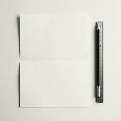 A blank folded sheet of paper beside a pencil and a steel ruler.